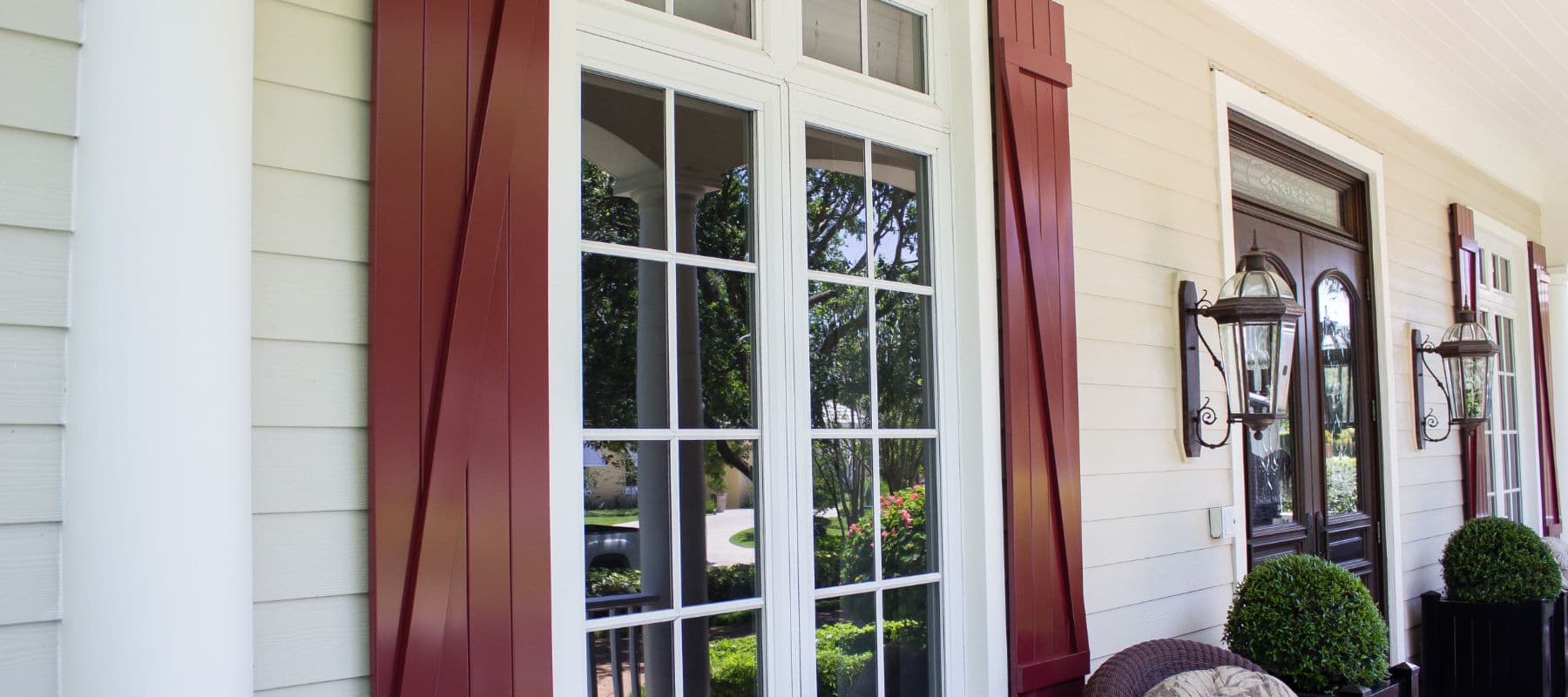 A close-up of a house front with maroon shutters, large grid windows, and decorative lanterns