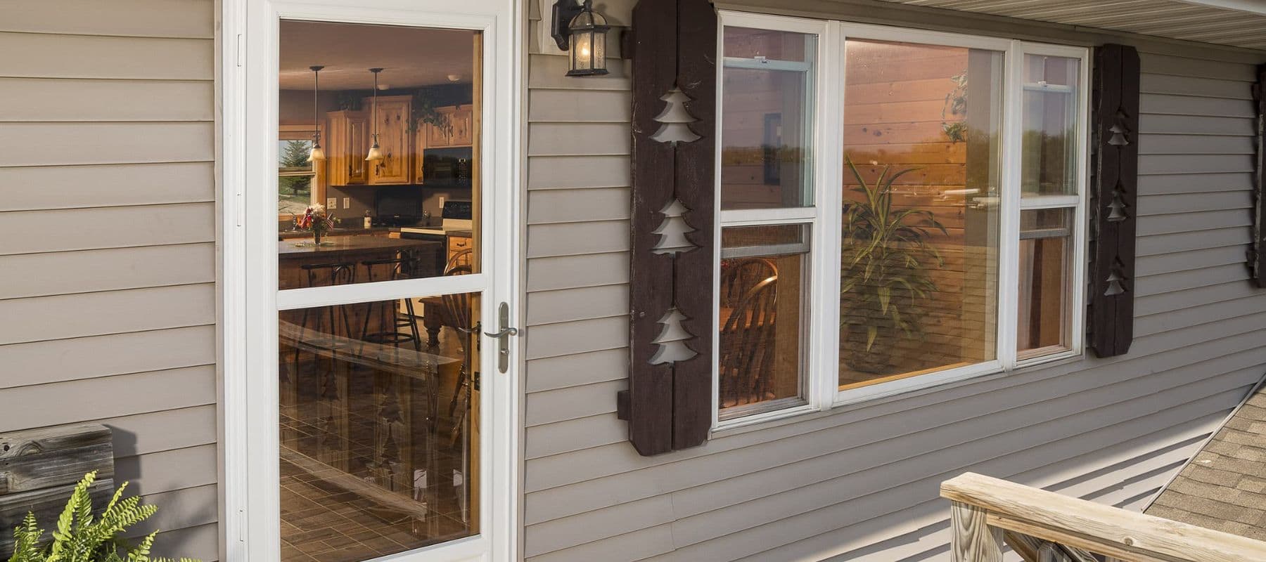 A beige house with a white-framed storm door and decorative shutters featuring pine tree cutouts