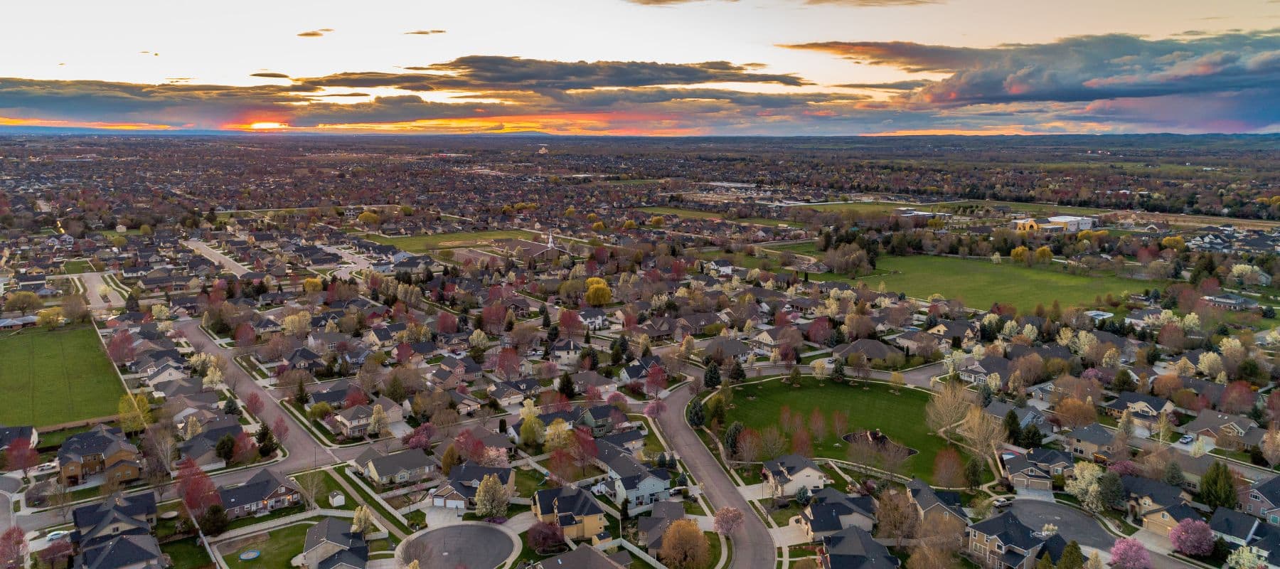 Aerial view of a sprawling suburban neighborhood at sunset with houses, streets, and trees