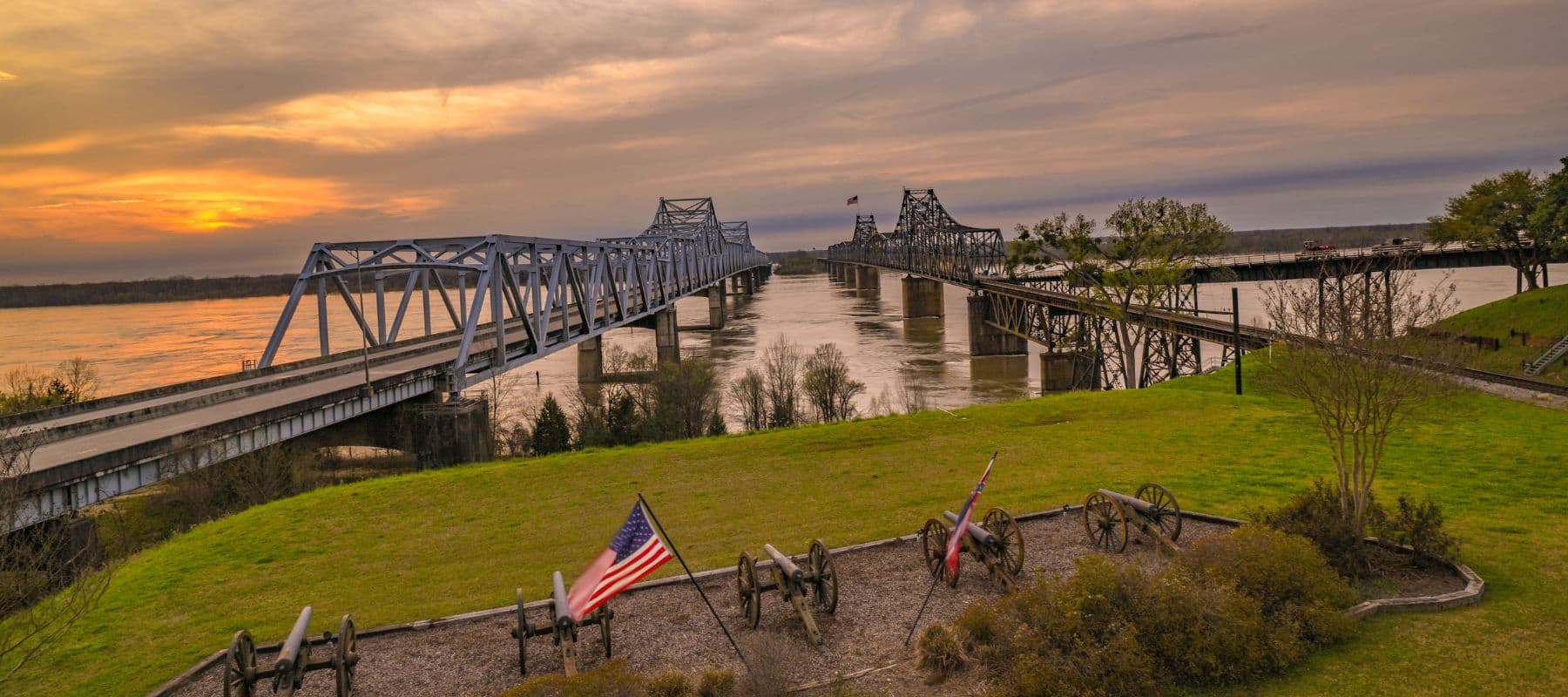 Historic cannons and American flags on a bluff overlooking twin bridges spanning the Mississippi River
