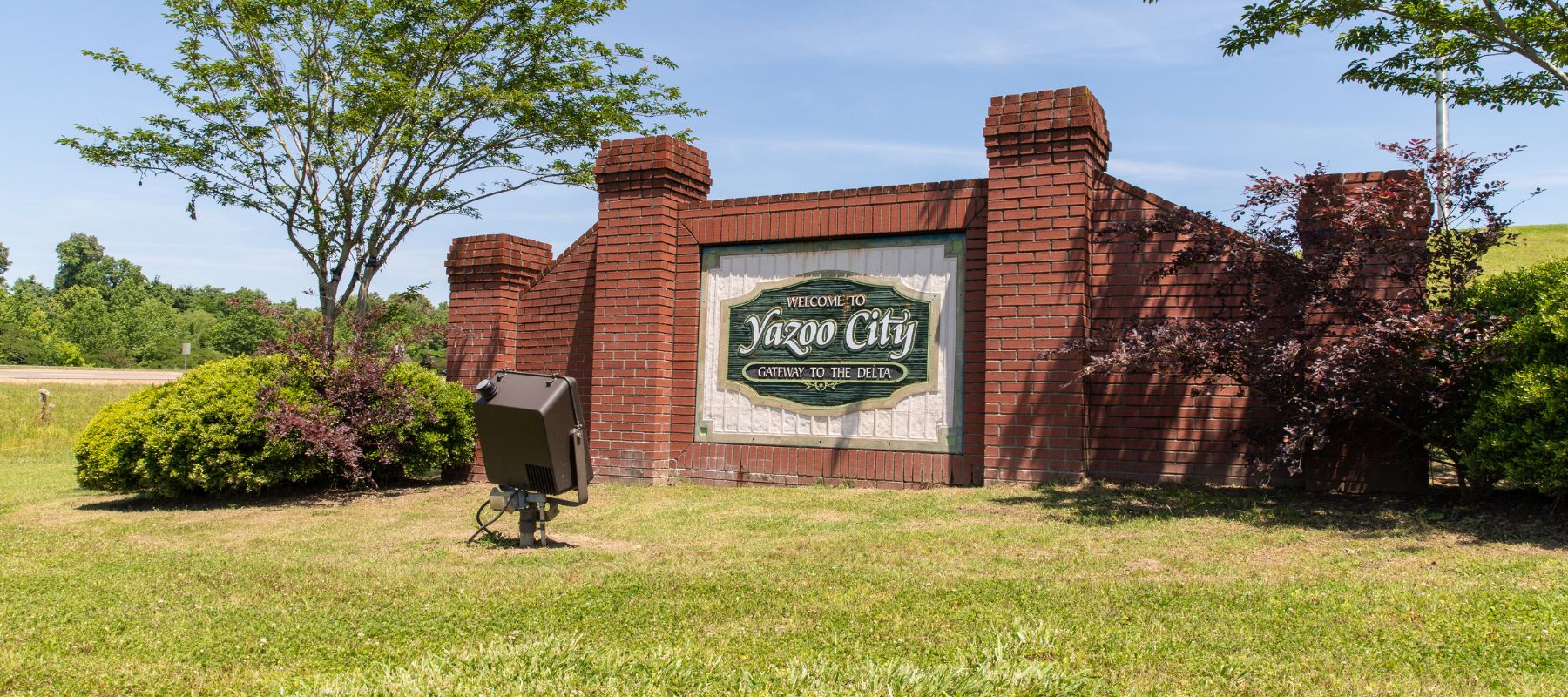 Welcome sign for Yazoo City, Mississippi mounted on a red brick wall with surrounding greenery
