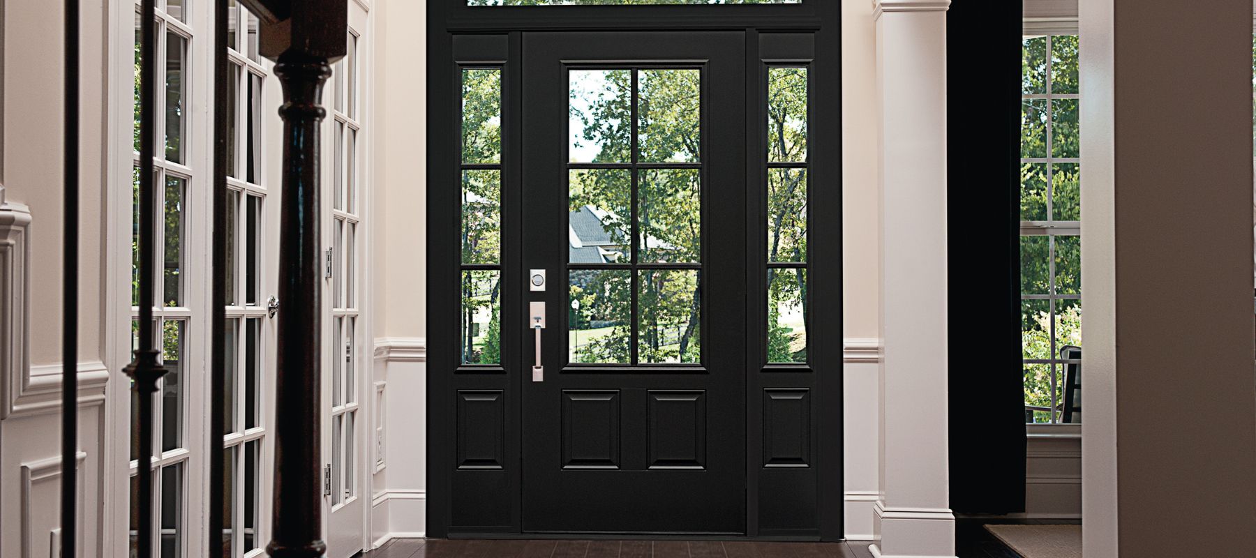 A stylish black front door with glass panes and side windows opens into a bright interior with white trim and a staircase
