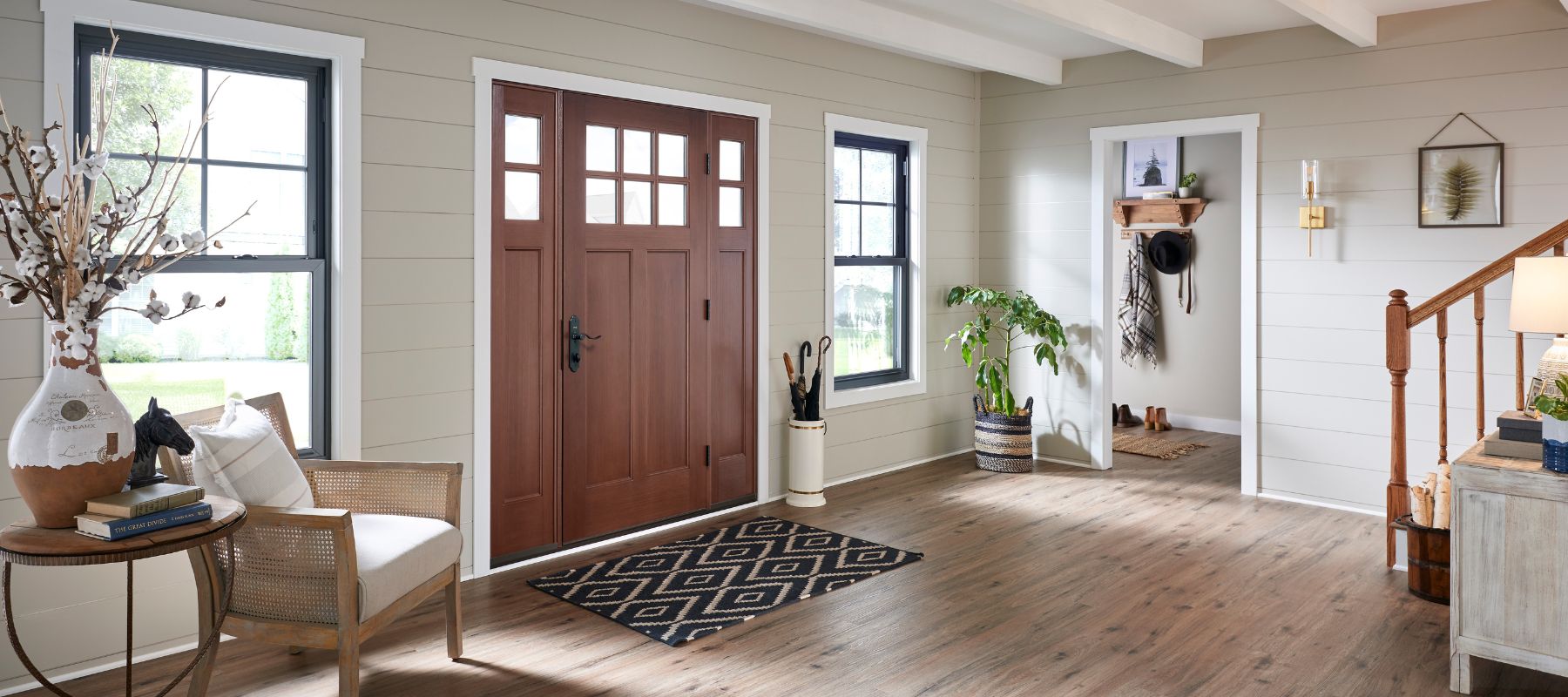 A welcoming entryway features a dark wood front door with glass panes, flanked by large windows, with light-colored walls and hardwood floors, and decorative elements throughout